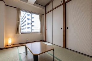A traditional Japanese room with tatami flooring, a low table, sliding doors, and a window with curtains.