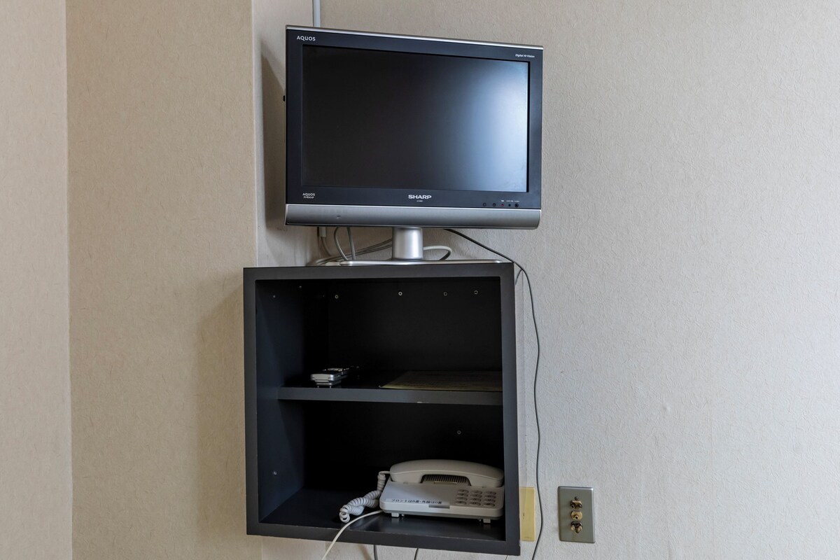 Uma televisão presa à parede e um telefone em um quarto com parede texturizada.