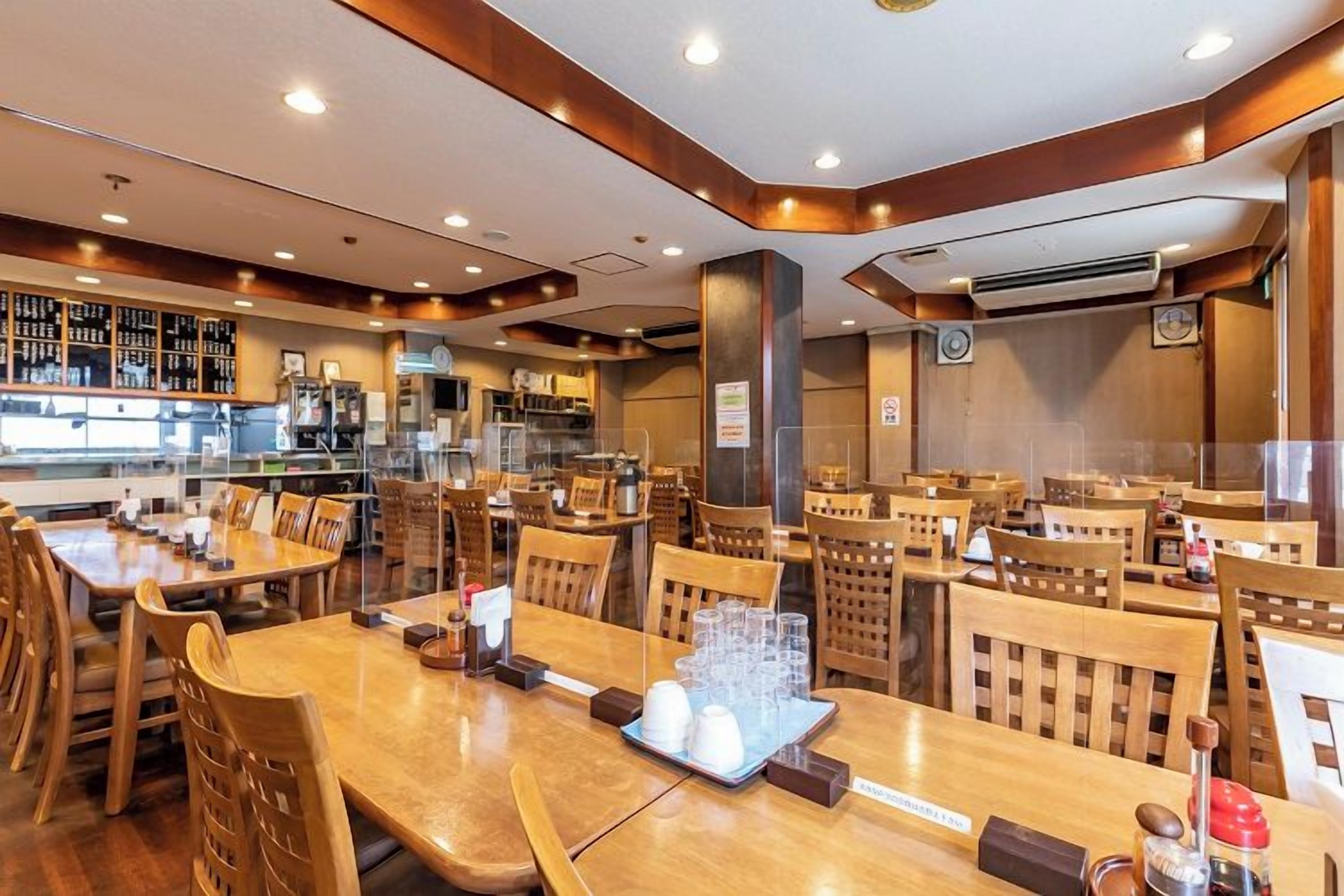 Un restaurante con mesas y sillas de madera, una zona de bar y una cocina al fondo.