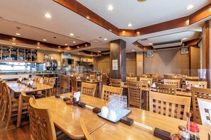 Un restaurante con mesas y sillas de madera, una zona de bar y una cocina al fondo.