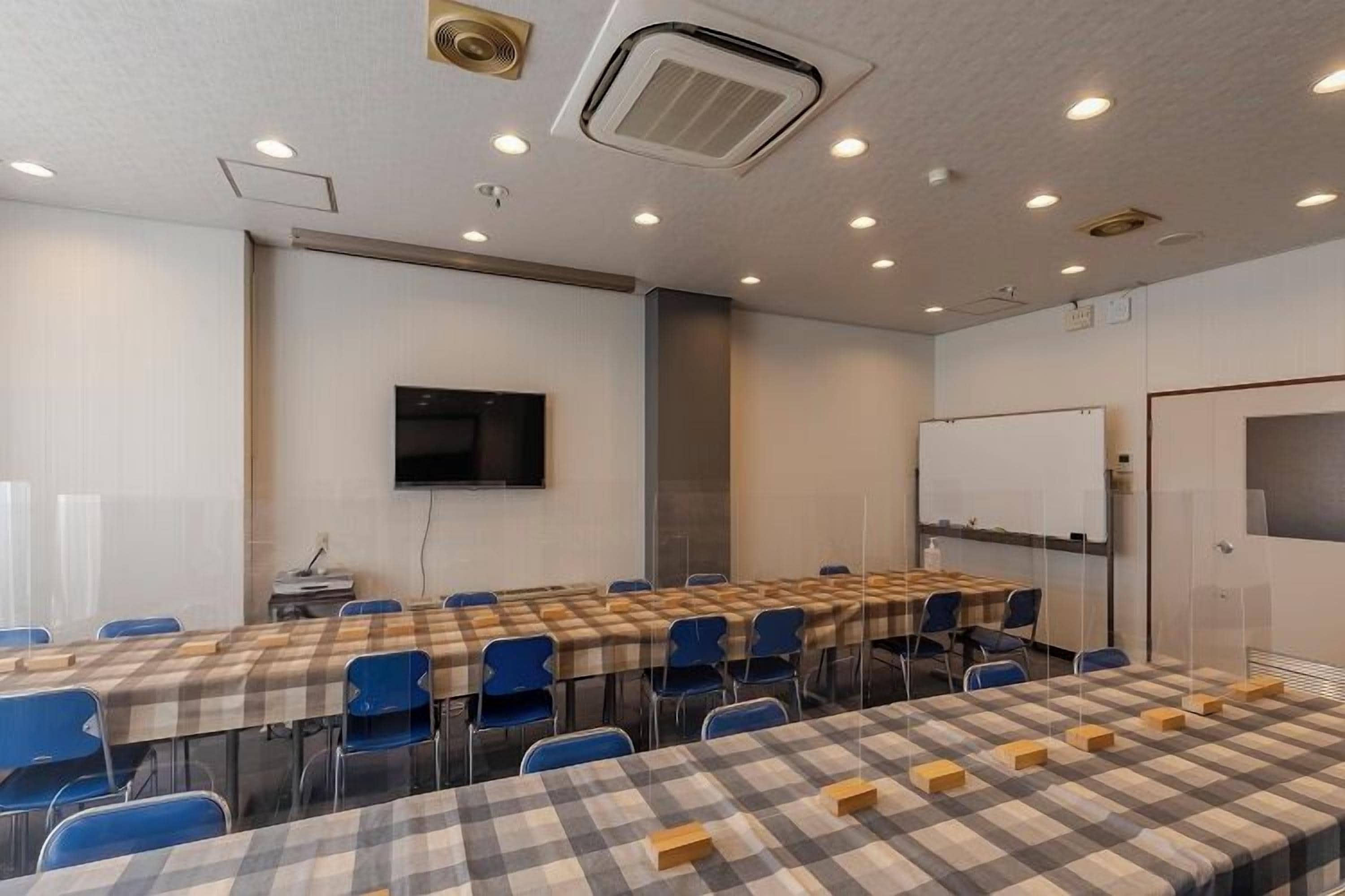 A conference room with tables, chairs, a whiteboard, and a television.