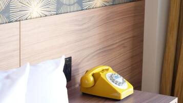 A wooden nightstand with a yellow rotary phone, a white pillow, and a pen on a piece of paper.