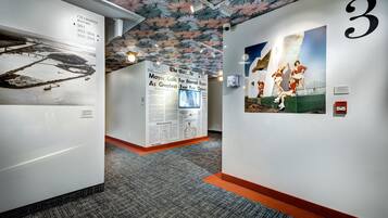 Un pasillo con un techo decorado con un diseño de hojas, una pared con el número grande '3', y una exhibición de un artículo de periódico sobre una exposición.