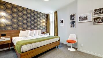 Una habitación de hotel moderna con una cama grande, una mesita de noche, una silla y una pared decorada con cuadros.