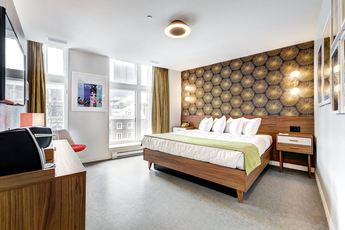 Une chambre d’hôtel moderne, dotée d’un grand lit, d’un bureau et offrant une vue sur la ville grâce à de grandes fenêtres.