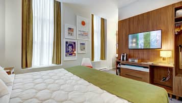 A hotel room with a large bed, a wooden desk, a television, and a window with curtains.