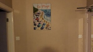 Una habitación con pared color beige, un radiador y un cuadro titulado 'La Plage'.