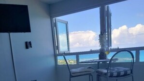 Een balkon met uitzicht op de lucht en wolken, een metalen stoel, een kleine tafel met een plant en een bank waarop het woord 'PEACE' staat.