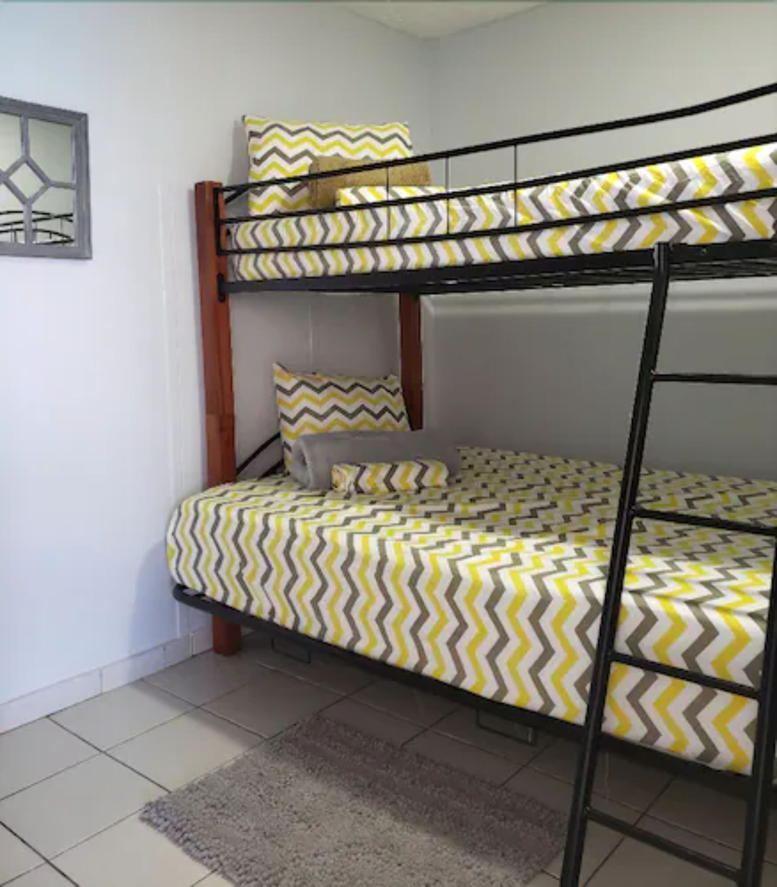 Een stapelbed met een bedsprei met een patroon, een grijze vloerkleed en een lijst met een afbeelding erop.