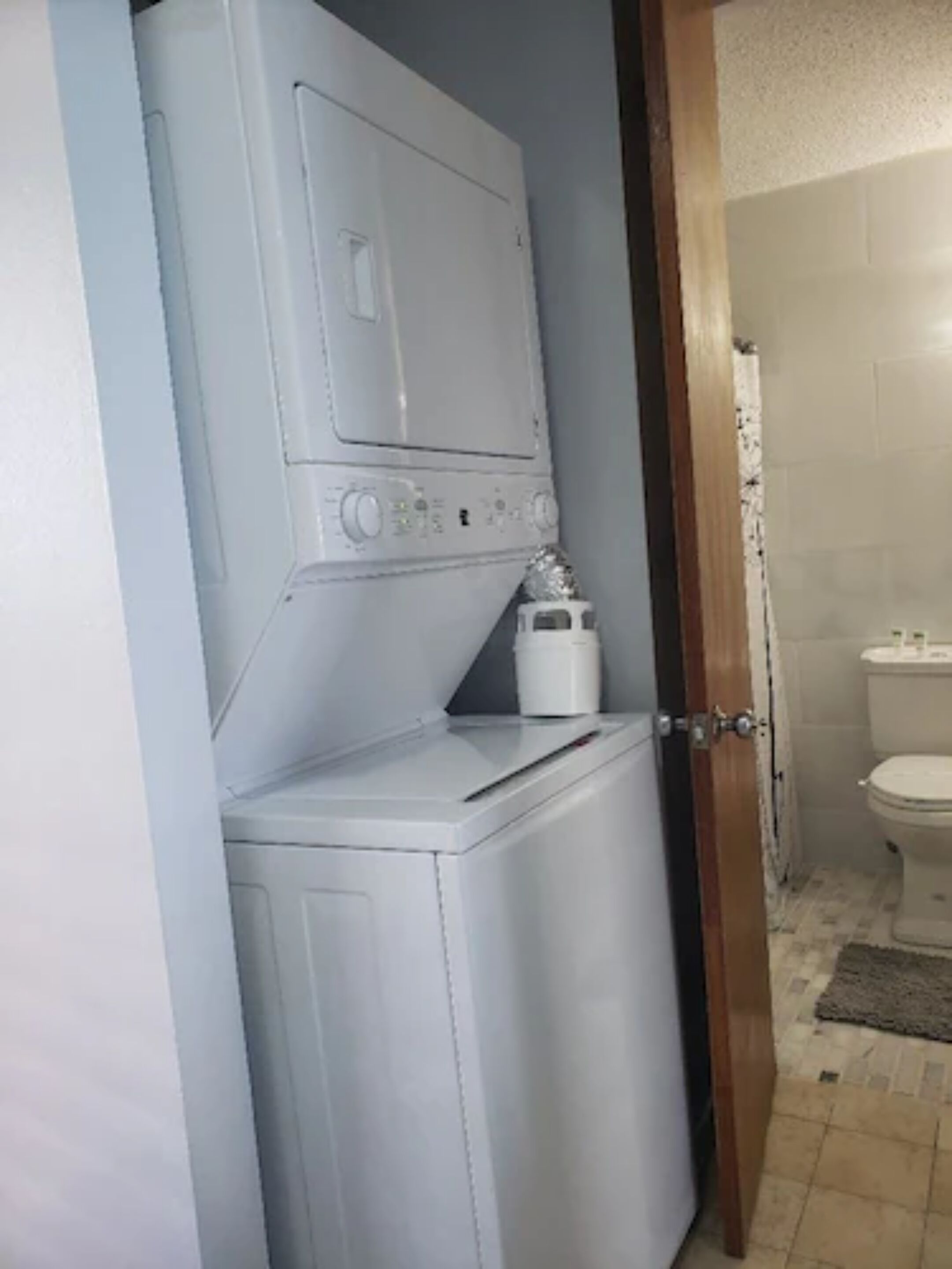 Ein kleiner Hauswirtschaftsraum mit Waschmaschine und Trockner, einem kleinen weißen Schrank und einer Toilette, die durch eine offene Tür sichtbar ist.