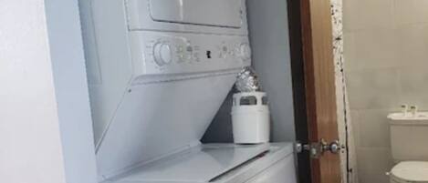 Ein kleiner Hauswirtschaftsraum mit Waschmaschine und Trockner, einem kleinen weißen Schrank und einer Toilette, die durch eine offene Tür sichtbar ist.