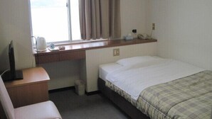 Ein Hotelzimmer mit Bett, Schreibtisch mit Telefon, Stuhl, Fenster mit Vorhängen und einer kleinen Mülleimer.
