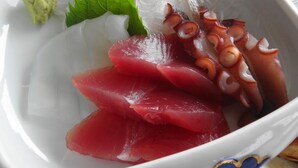 Eine Schüssel mit Sashimi, darunter Oktopus und Fischscheiben, dekoriert mit grünen Blättern und Wasabi.