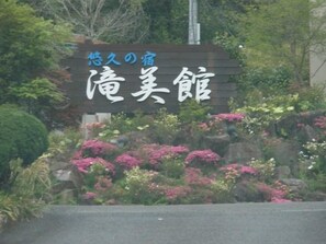 Un cartel con caracteres japoneses, rodeado de exuberante follaje y flores rosadas.