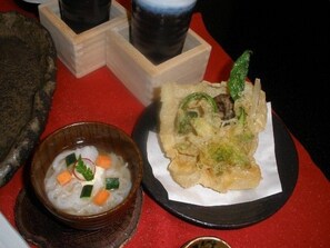Un tazón de sopa con vegetales y un plato de comida frita con guarniciones verdes.