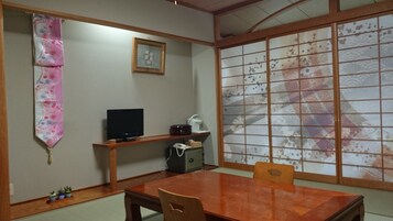 Una habitación japonesa tradicional con suelo de tatami, una mesa de madera baja, un televisor y un divisor shoji.