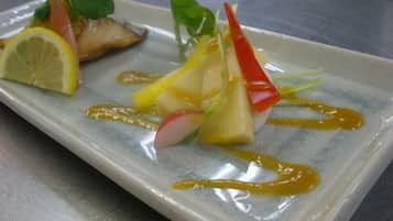 A rectangular plate with a dish consisting of a slice of fish, lemon, radish, and a red vegetable, possibly a chili pepper, with a drizzle of sauce.