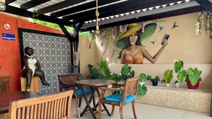 Un espace extérieur aménagé, abrité et doté d’une fresque murale, de mobilier en bois et de plantes en pot.