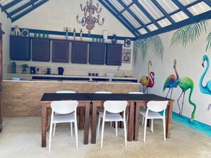 A kitchen with wooden cabinets, a dining table with chairs, a chandelier, and a mural of flamingos. - Casa Amalia (Jan Thiel)