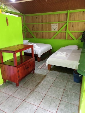 Una habitación con dos camas, una mesa de madera y una pared verde.