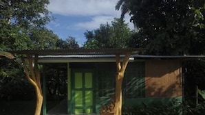Una pequeña estructura de madera con una puerta verde, un banco y un espacio cubierto con techo.