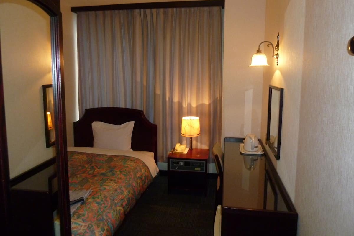 A hotel room with a bed, a desk with a lamp, a telephone, and a mirror.