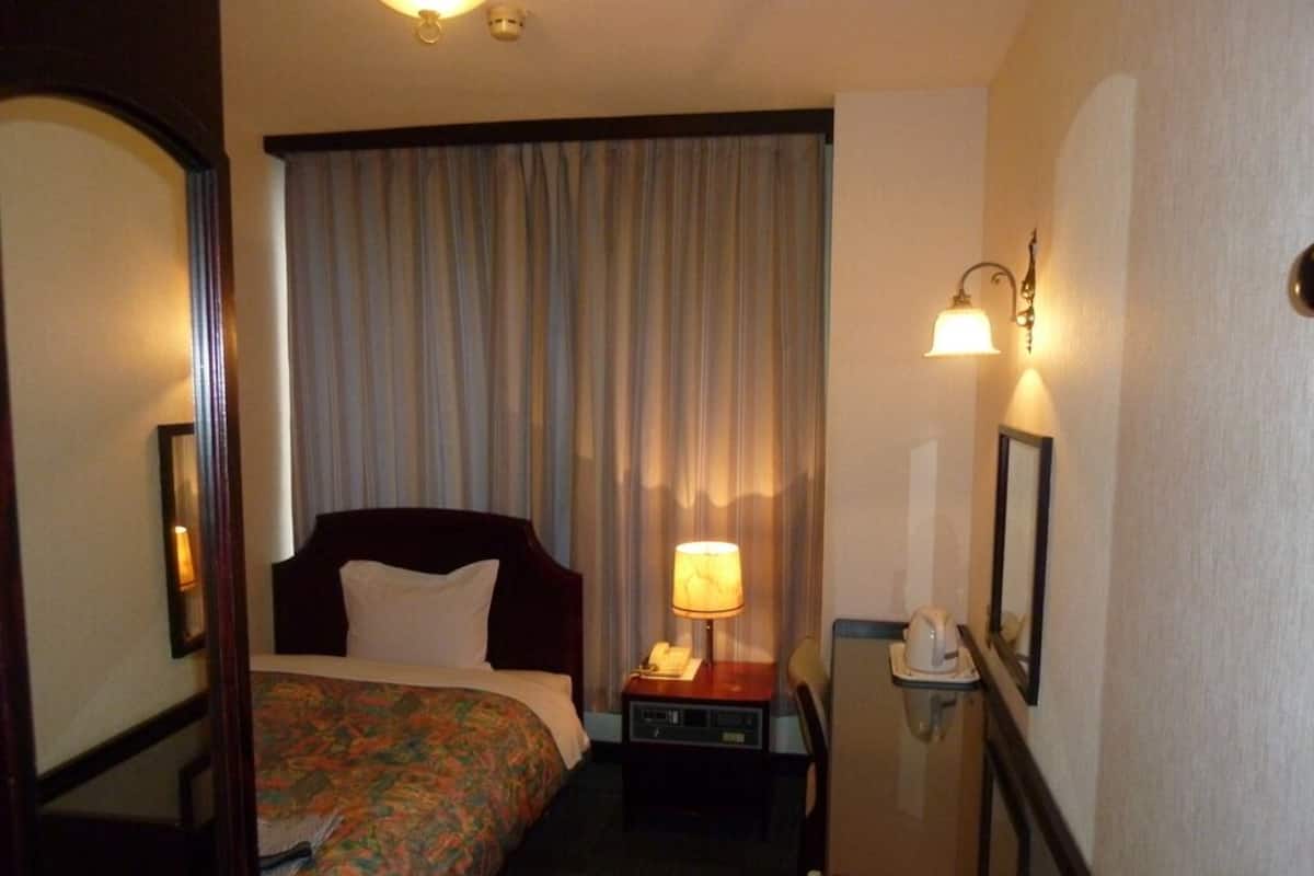 A hotel room with a bed, bedside table with a lamp, a telephone, and a mirror on the wall.