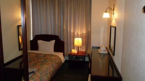 Una camera d'albergo con un letto, una scrivania con lampada, un telefono e uno specchio.