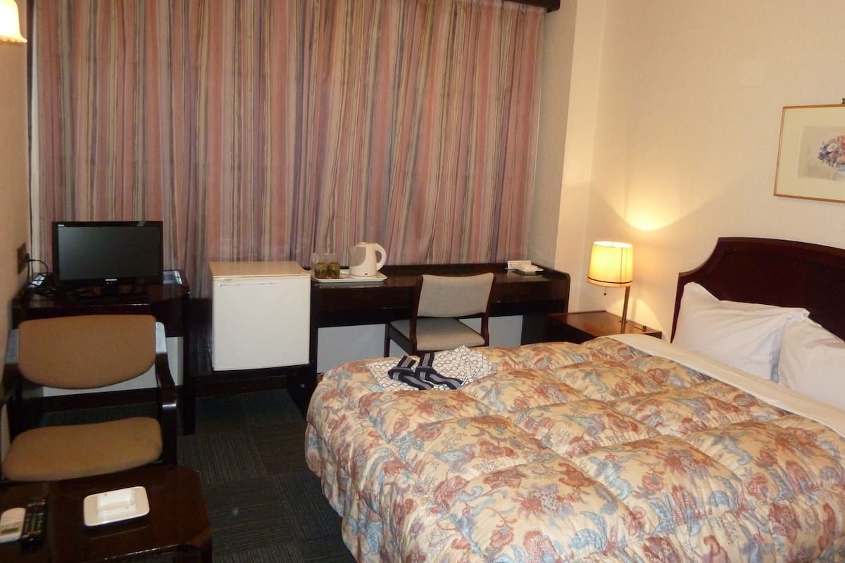 A hotel room with a bed, desk, chair, television, and a coffee maker.