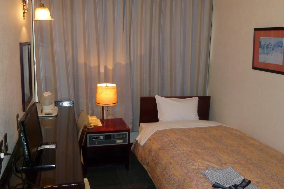 A hotel room with a bed, a desk with a telephone, a lamp, and a television.