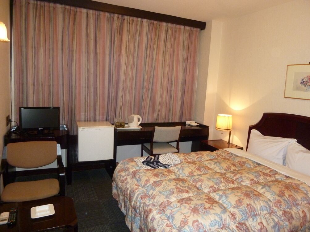 A hotel room with a bed, desk, chair, television, and a small refrigerator.