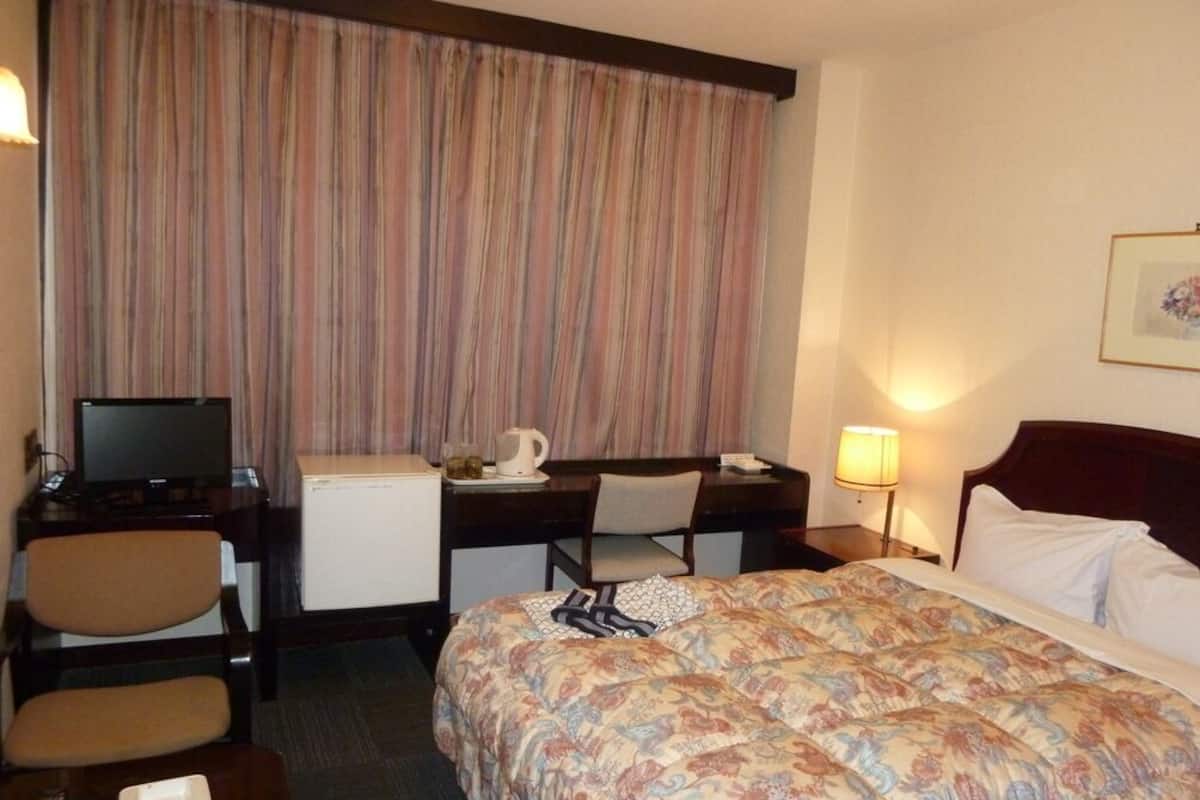 A hotel room with a bed, desk, chair, television, and a small refrigerator.
