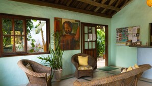 A room with wicker furniture, a large potted plant, and a wall with a bulletin board. - Atmosphera Pousada (Porto Seguro)