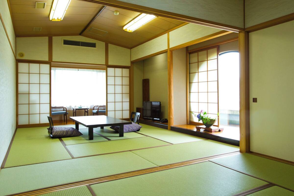 A traditional Japanese room with tatami flooring, a low table, chairs, a television, and sliding doors.
