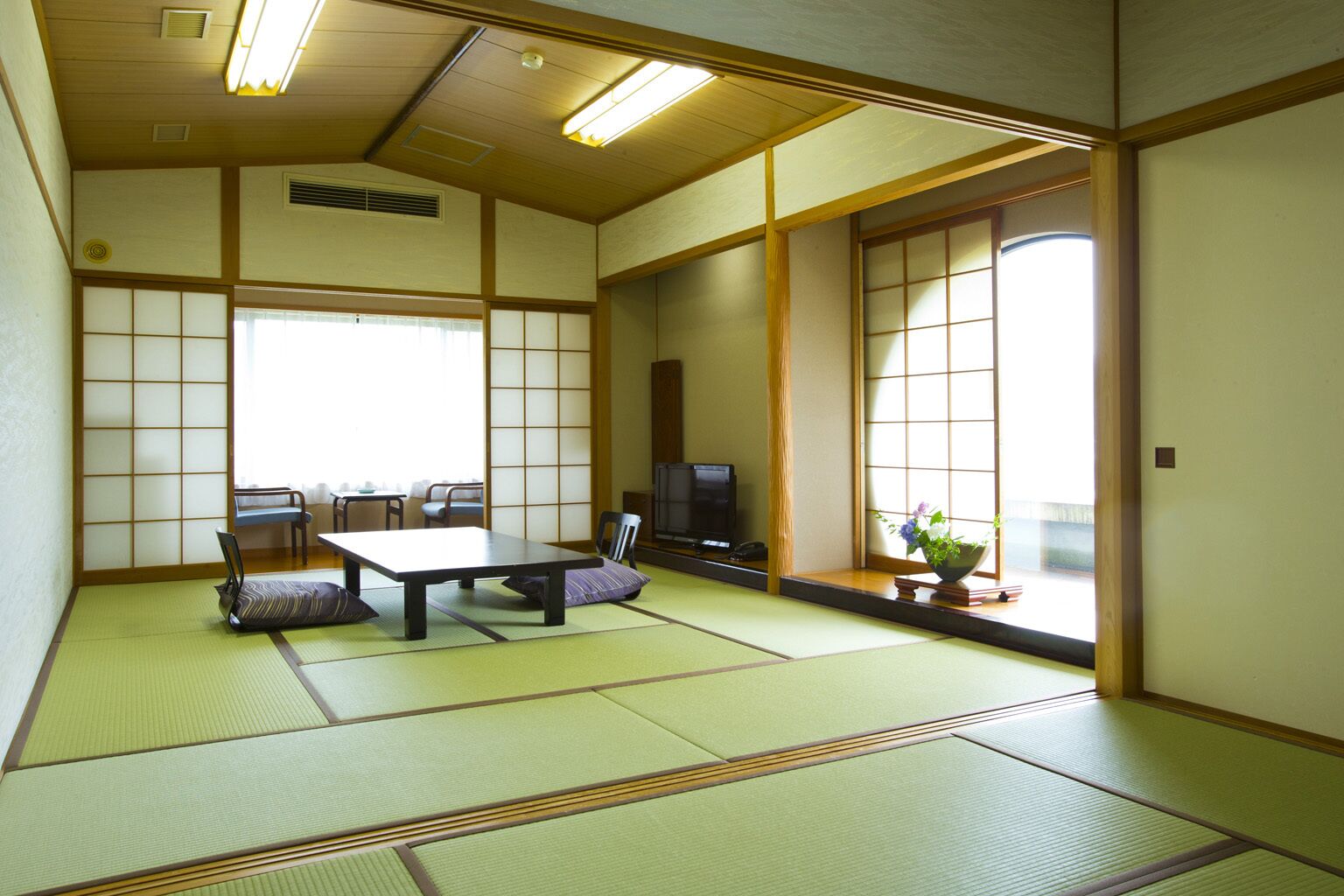 A traditional Japanese room with tatami flooring, a low table, chairs, a television, and sliding doors.