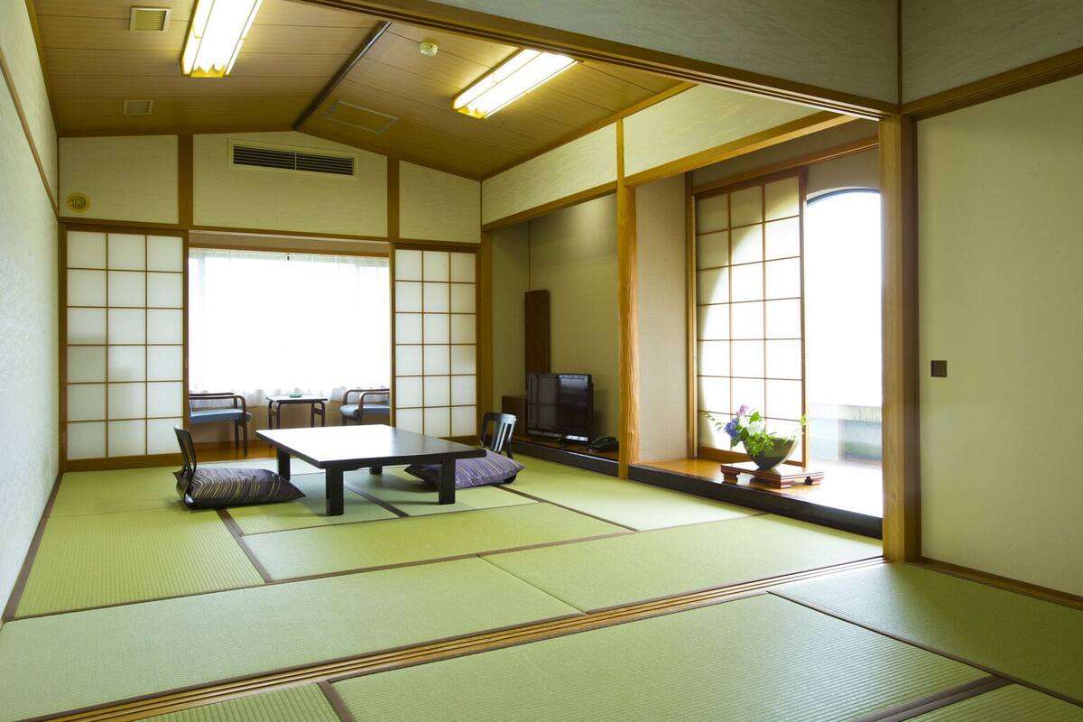 A traditional Japanese room with tatami flooring, a low table, chairs, a television, and sliding doors.