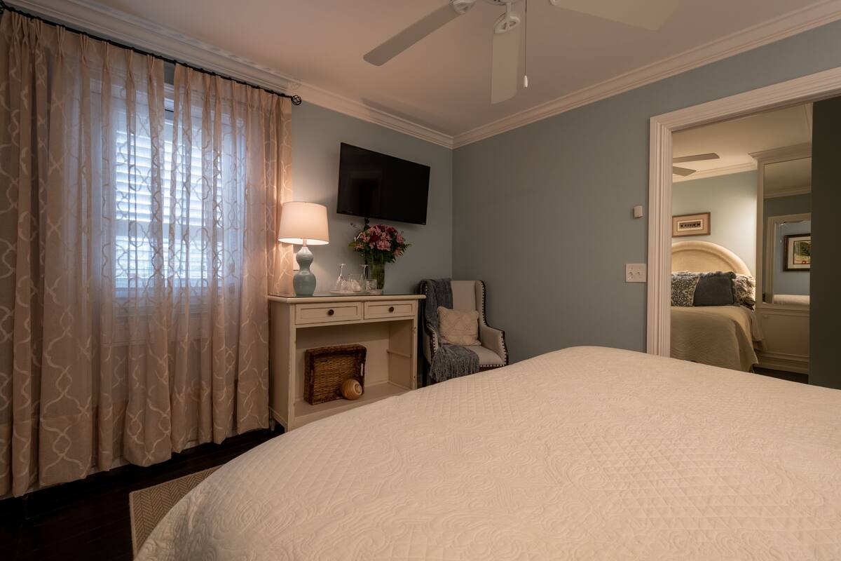 A bedroom with a bed, a desk, a chair, a TV, and a mirror.