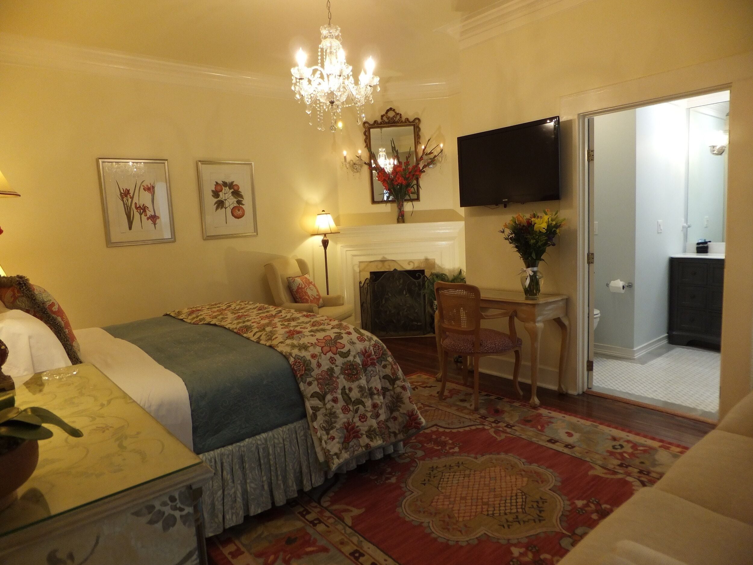 Habitación de hotel con una cama, un escritorio, una silla, un televisor, una chimenea y una puerta que da a un baño.