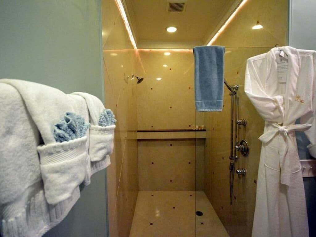 A glass-enclosed shower area with a towel rack holding a blue towel and a white robe.