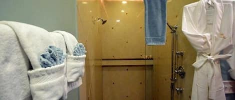 A glass-enclosed shower area with a towel rack holding a blue towel and a white robe.