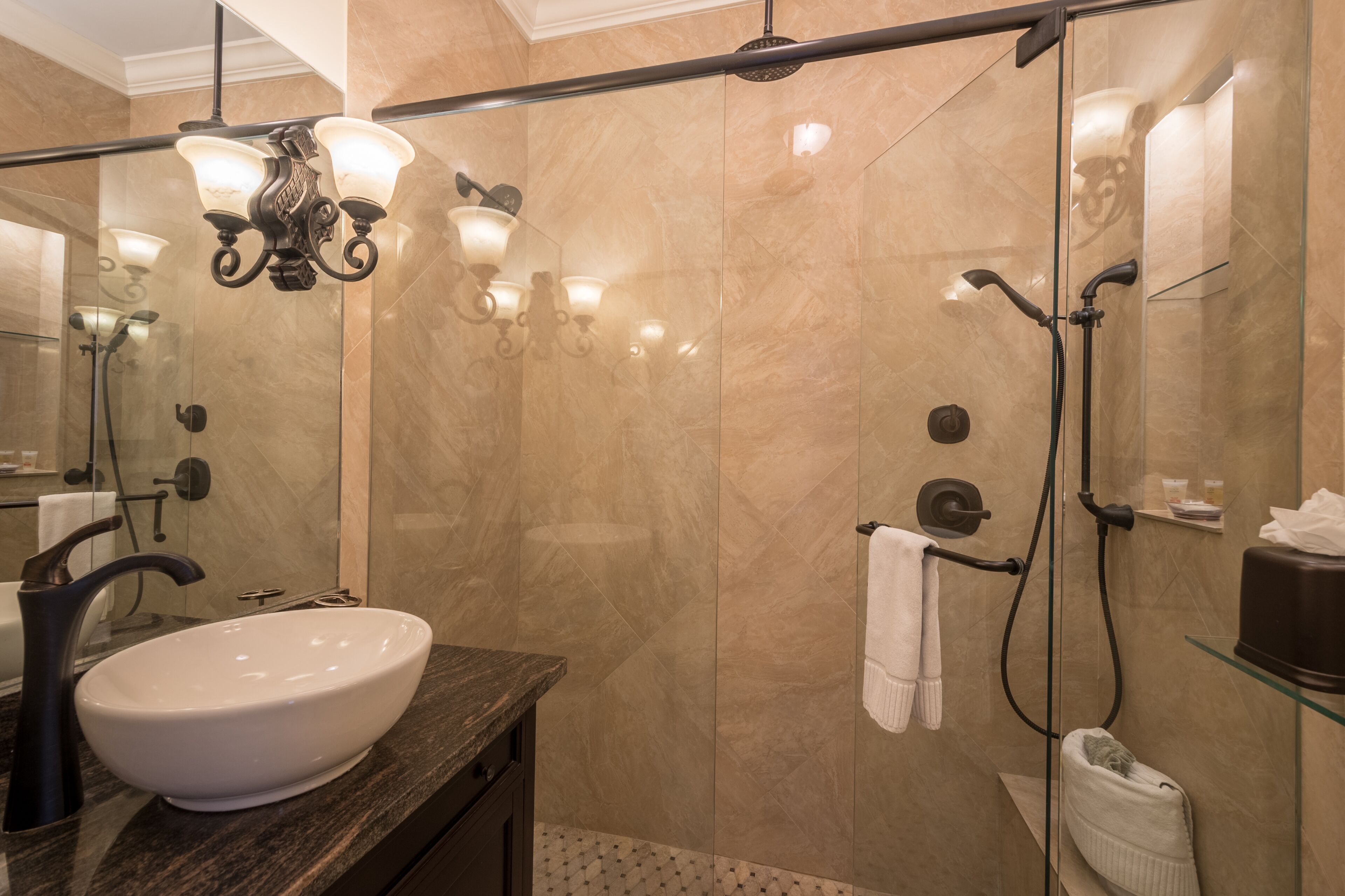 Een moderne badkamer met een groot wit wastafel, donker aanrechtblad en een douchecabine van glas.