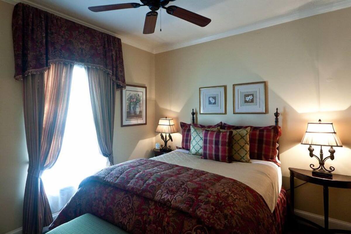 A hotel room with a bed, a ceiling fan, two bedside lamps, and a window with curtains.