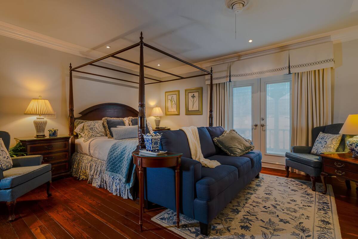 A four-poster bed with a dark headboard, a blue sofa, and a matching armchair.