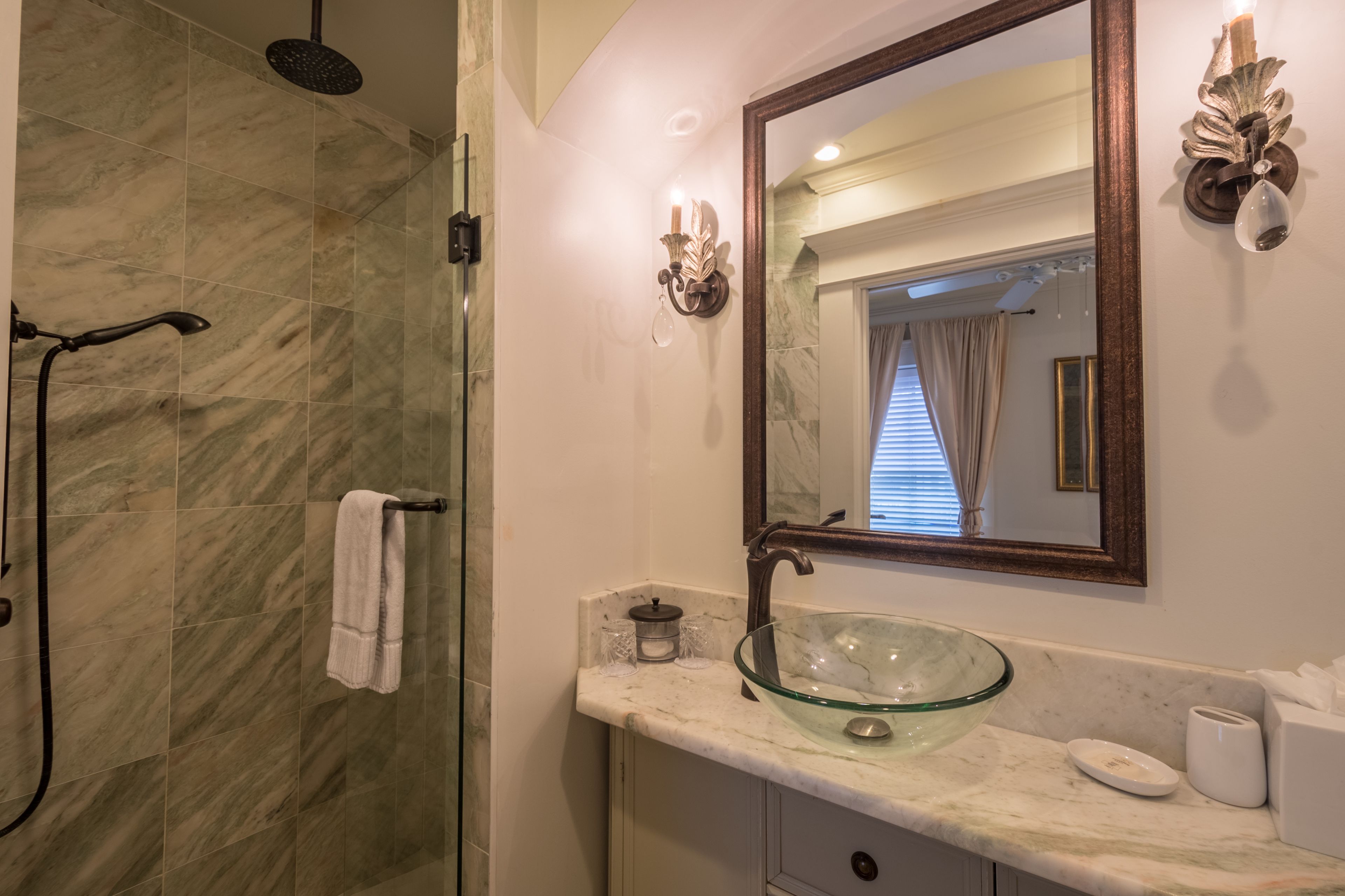 A bathroom with a glass bowl sink, a shower, and a mirror with wall sconces.