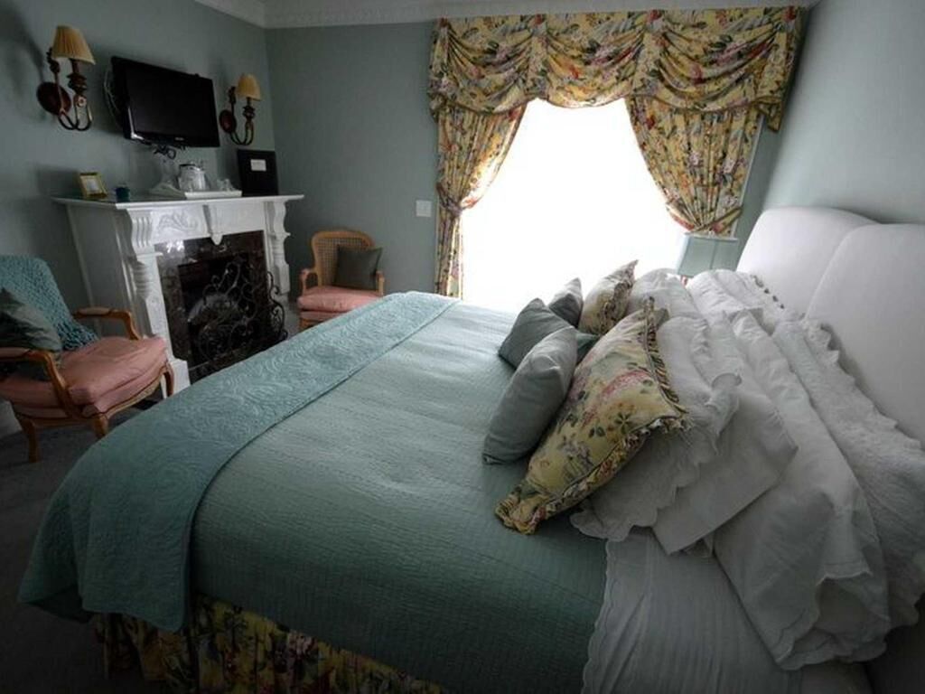 A bedroom with a bed, a fireplace, a television, and a window with curtains.