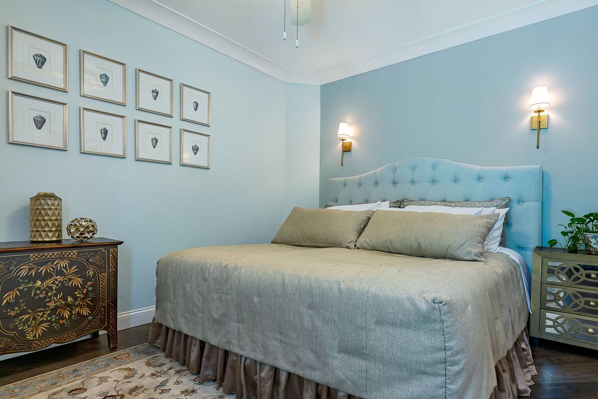 A bedroom with a large bed, a nightstand with a lamp, a dresser, and framed pictures on the wall.