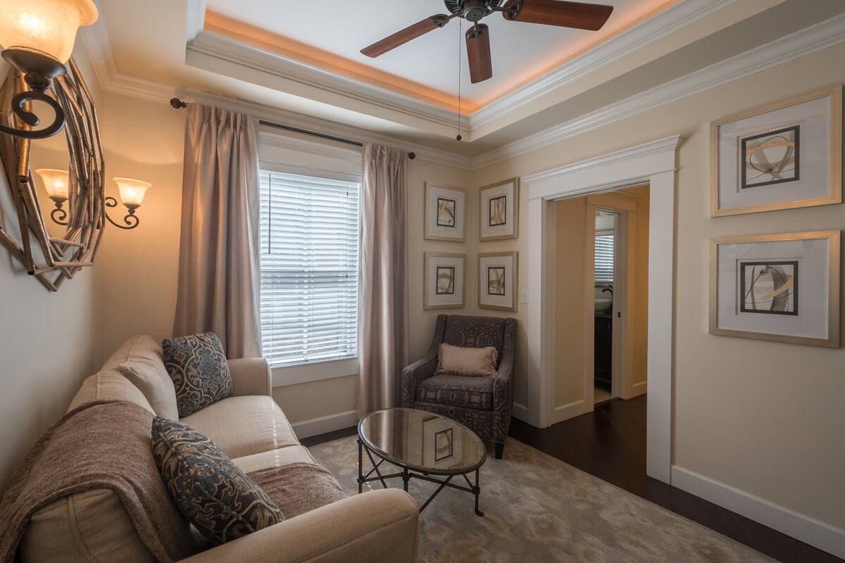 A living room with a sofa, a coffee table, a patterned armchair, and a ceiling fan.