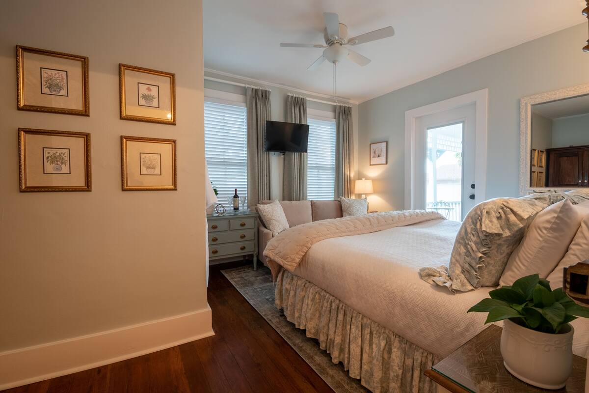 A bedroom with a large bed, a ceiling fan, a TV, and framed pictures on the wall.