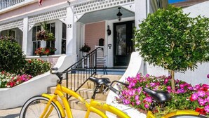A yellow bicycle parked in front of a building with a white facade, a porch with potted plants, and a staircase leading to the entrance. - The Kenwood Inn (St. Augustine)