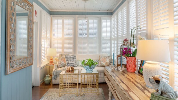 A cozy room with a ceiling fan, a large mirror, a sofa with cushions, a coffee table, and a side table with a lamp and decorative items. - The Kenwood Inn (St. Augustine)